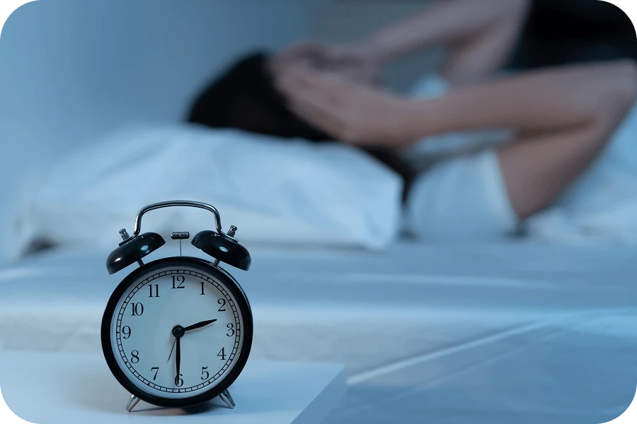 夜中に目が覚める不眠の悩みを連想させる目覚まし時計とベッドの人物の写真