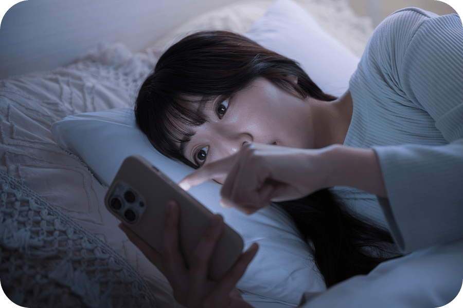 暗い寝室で就寝前にスマートフォンの強い光を浴びる人の写真